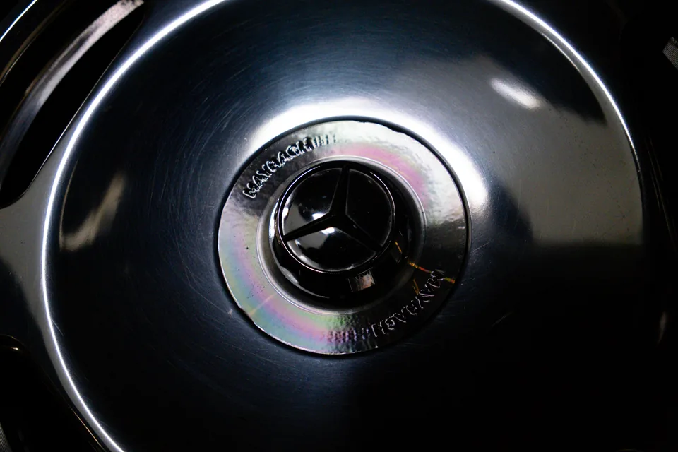 Close view of a polished wheel centre cap bearing a three-pointed star emblem, with light curving across the rim