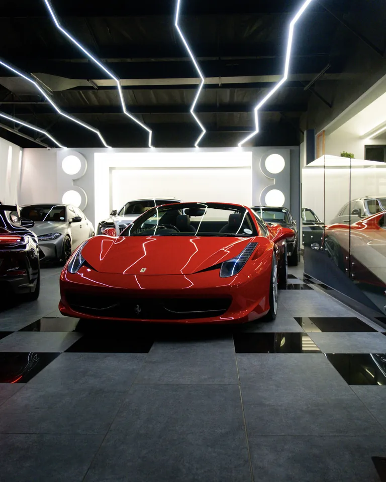Red Ferrari 458 Spider facing forward in a showroom, light reflecting along its bonnet, other cars parked behind