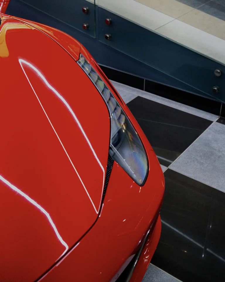 Close view of a red Ferrari 458 Spider headlight and the curve of its glossy bonnet on a chequered showroom floor
