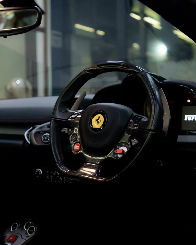 Ferrari steering wheel with a yellow prancing-horse badge, red start button and carbon details, seen from the driver's seat