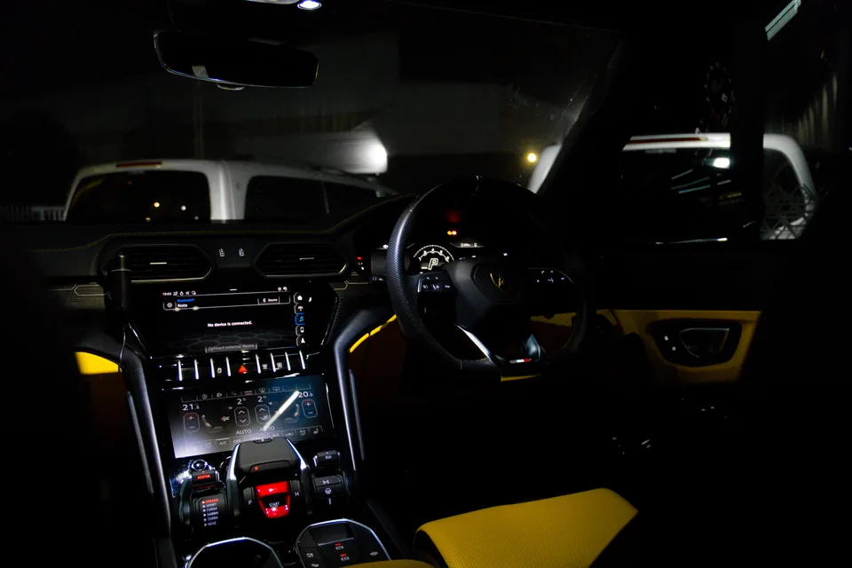 Lamborghini Urus cockpit at night with glowing digital screens, a centre console and yellow seat accents