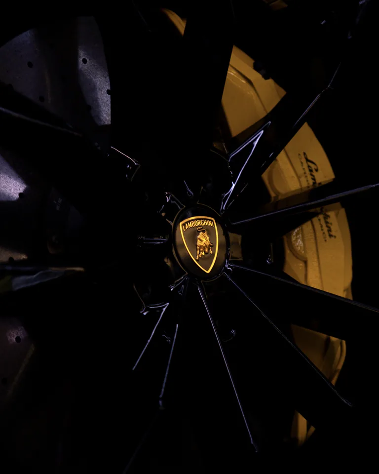 Dark multi-spoke Lamborghini wheel with an illuminated centre badge and a yellow brake caliper behind the spokes