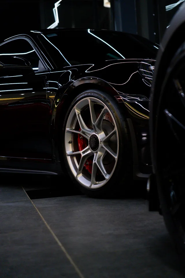Rear haunch of a black Porsche 911 GT3 with a silver centre-lock wheel and red caliper, light lines reflected in the paint