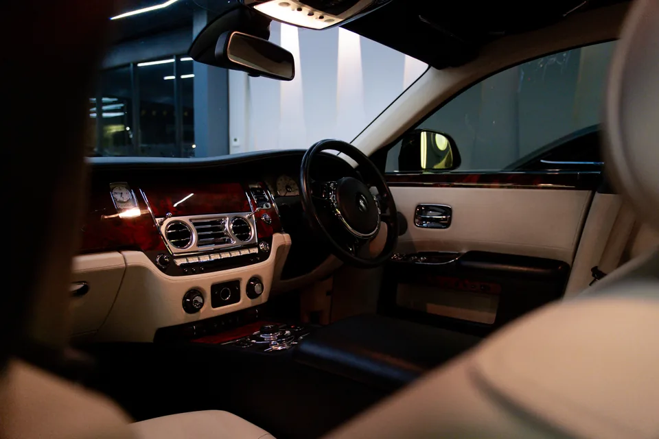 Rolls-Royce interior seen from the rear seat, with polished wood veneer dashboard, round air vents and cream leather