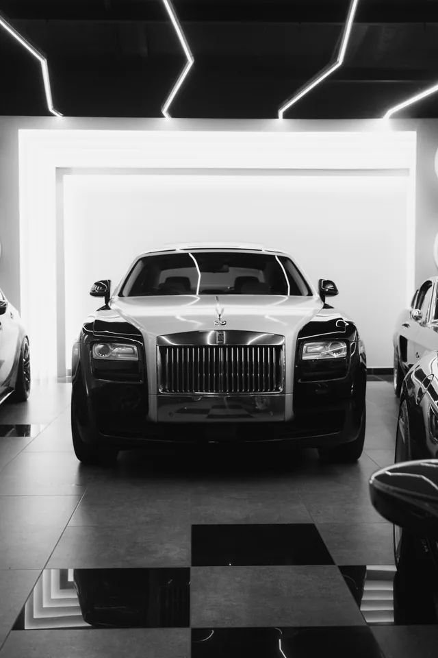 Black-and-white photograph of a Rolls-Royce Ghost facing the camera in a bright showroom with a chequered floor