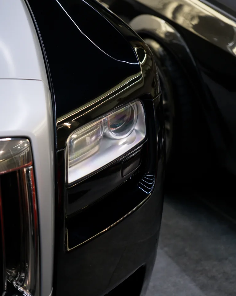 Close view of a Rolls-Royce headlight where silver and black paint meet on the front wing