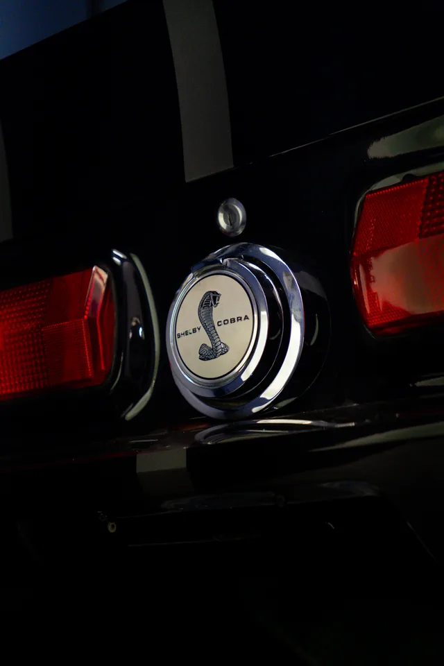 Chrome Shelby Cobra fuel cap set between the red tail lights of a dark 1967 Mustang Shelby GT500