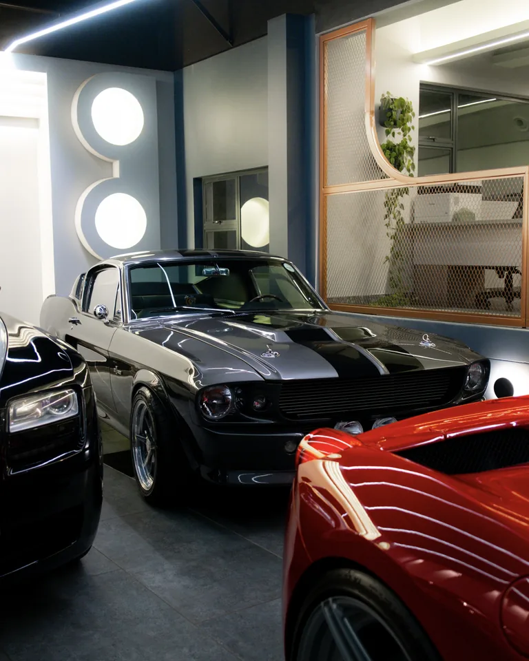 Grey 1967 Ford Mustang Shelby GT500 with black stripes, parked between the nose of a Rolls-Royce and a red Ferrari